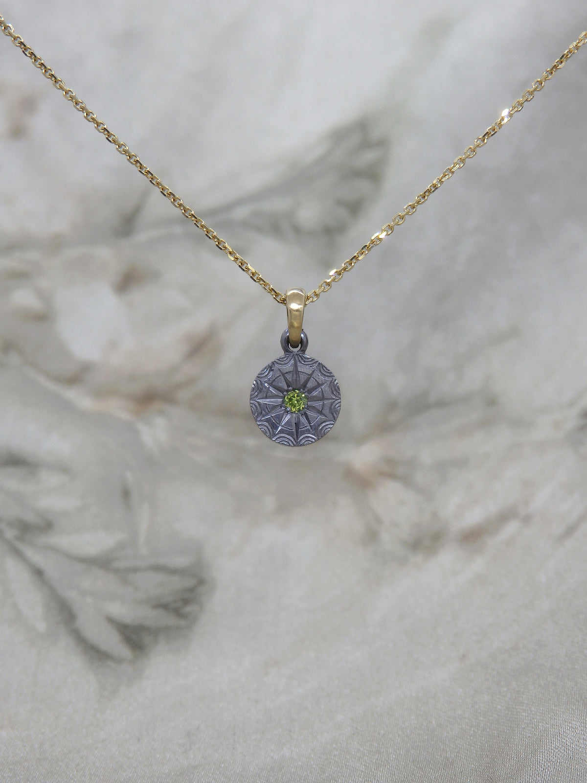 Green Australian sapphire pendant in hand-engraved pure tantalum with an 18ct yellow gold chain loop. The sapphire is set in a 12-pointed star with a ring around it, each point separated by an engraved ripple around the outside. 