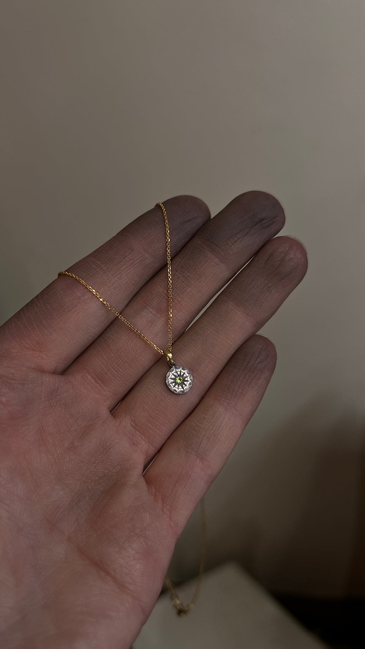Shown on an hand green Australian  sapphire pendant in hand-engraved pure tantalum with an 18ct yellow gold chain loop. The sapphire is set in a 12-pointed star with a ring around it, each point separated by an engraved ripple around the outside. 