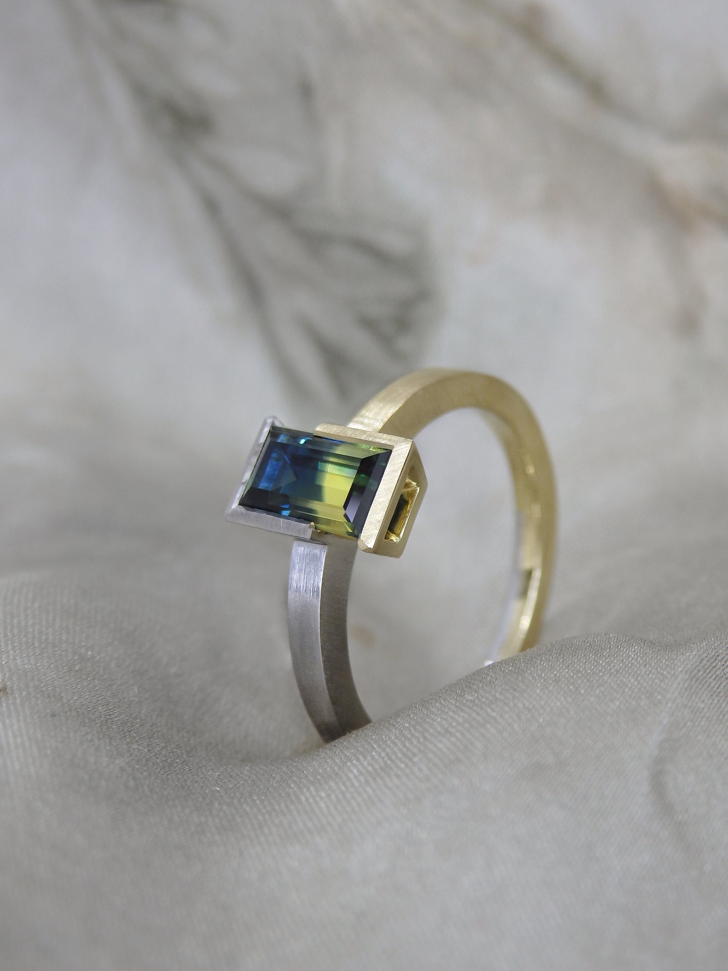 Side view of Bi colour baguette cut blue and yellow split Australian parti sapphire in two tone 18k yellow gold and platinum partial bezel solitaire engagement ring. Brushed matte finish with polished highlights