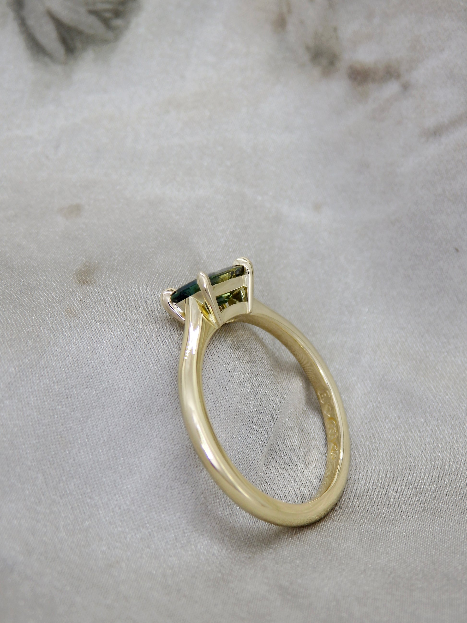 Side view of  a split bi-colour blue and yellow Australian baguette cut Parti Sapphire in an east-west across the finger four claw 18k yellow gold solitaire engagement ring with open light gallery with tapering claws 