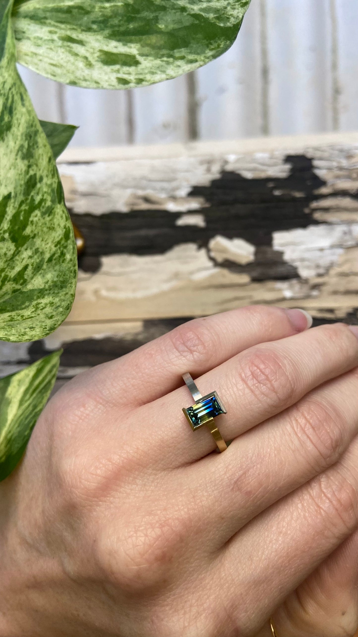 Bi colour baguette cut blue and yellow split Australian parti sapphire in two tone 18k yellow gold and platinum partial bezel solitaire engagement ring shown in left ring ring finger to show size and proportion. Brushed matte finish