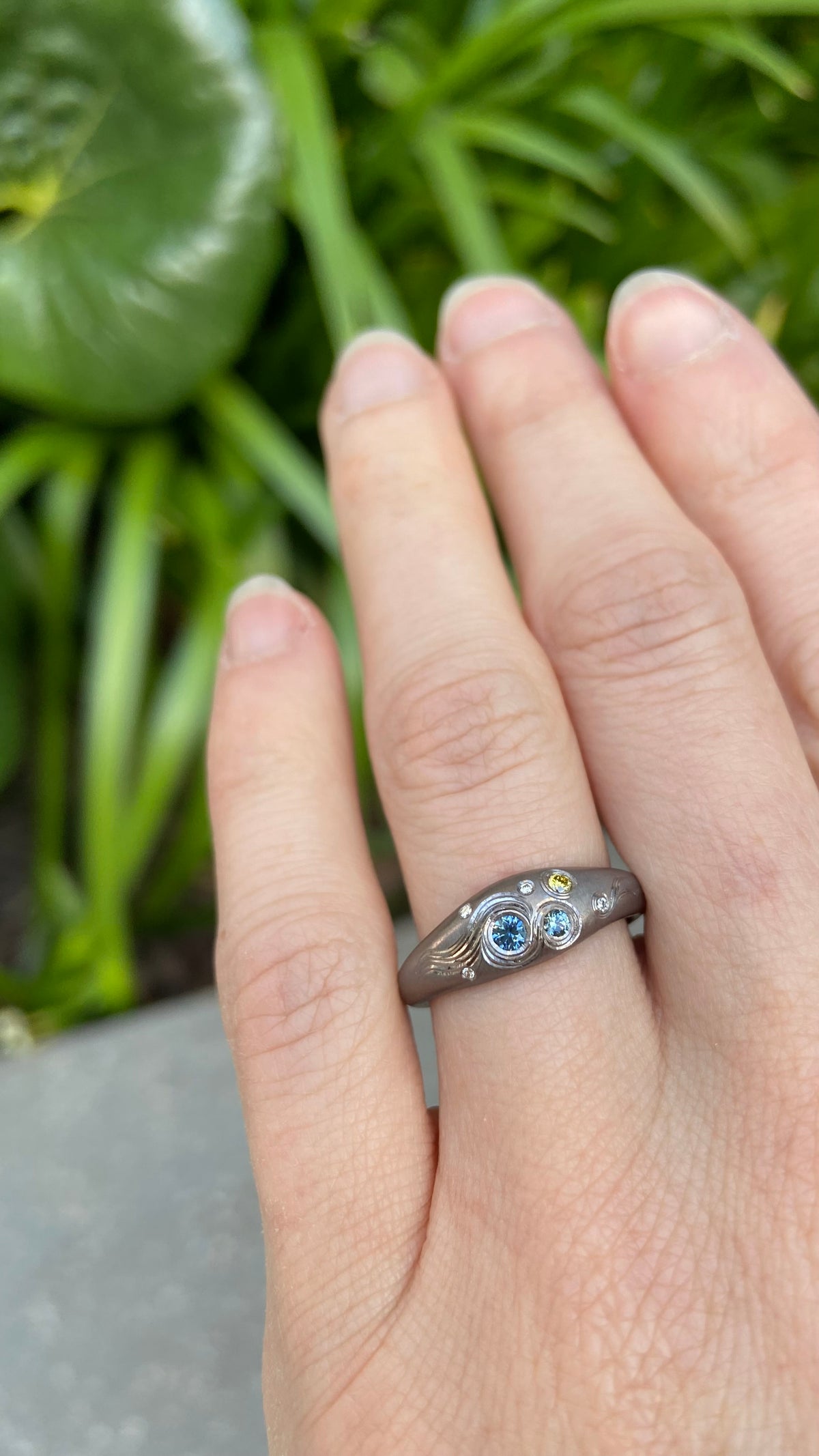 Shown on a finger, Hand Engraved black Tantalum Ring with australian parti sapphires and natural diamonds in a high domed tapering profile