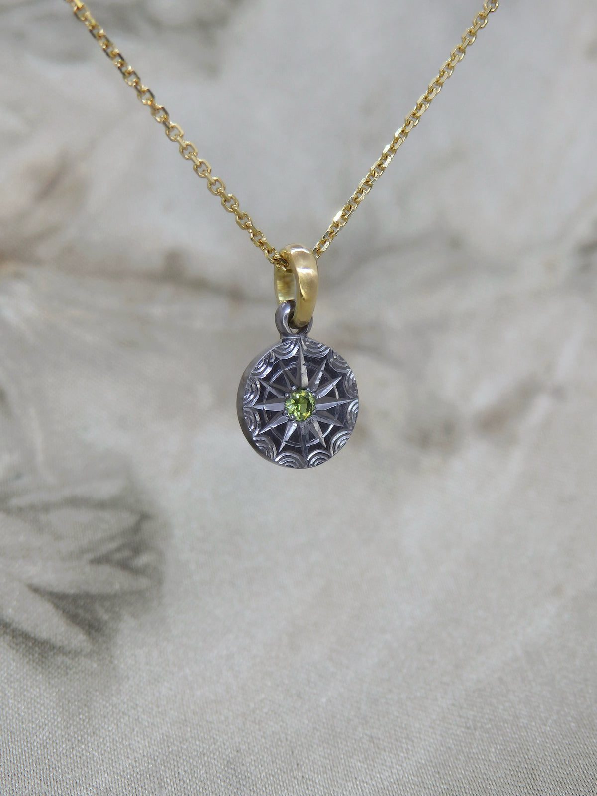 Australian sapphire pendant in hand-engraved pure tantalum with an 18ct yellow gold chain loop. The sapphire is set in a 12-pointed star with a ring around it, each point separated by an engraved ripple around the outside. 